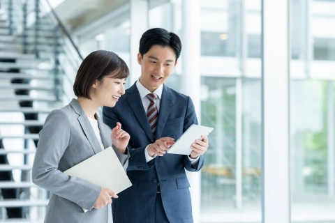 スーツ姿の男女2名がタブレットを見ながら笑顔で会話している