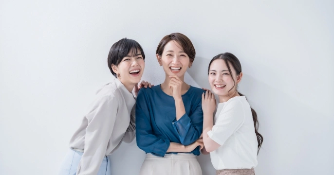 3名の女性が仲良く肩を組みながら笑っている