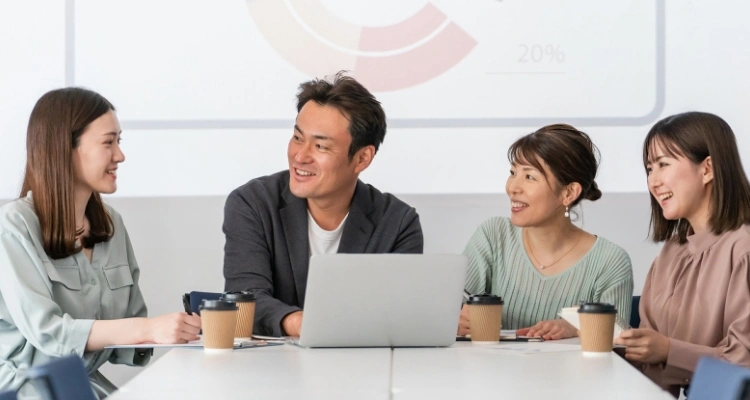 4名の男女がラップトップPCを囲んで楽しそうに会議している