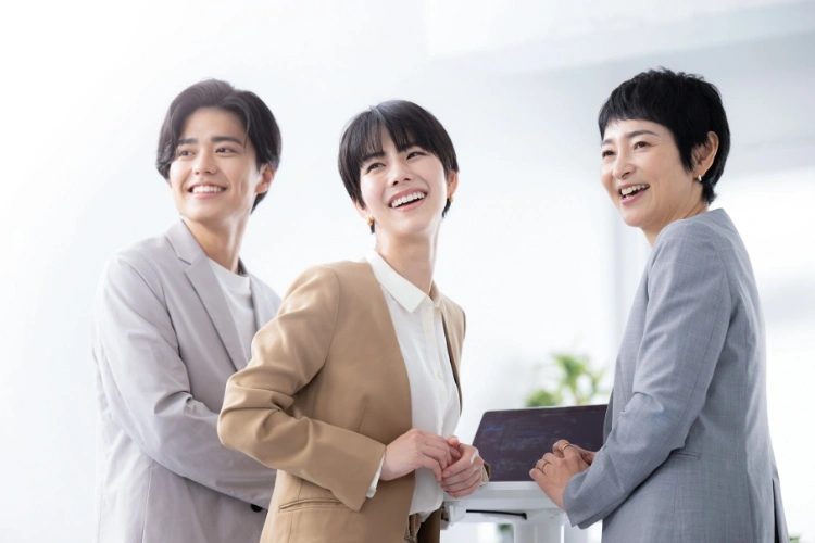 3人の男女がカジュアルなビジネスファッションで、明るい笑顔を見せている