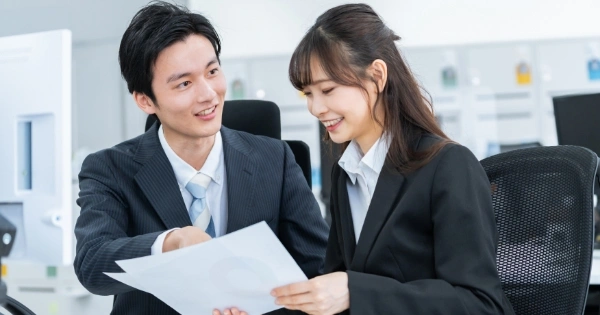 オフィスで資料を見ながら会話しているスーツ姿の男女